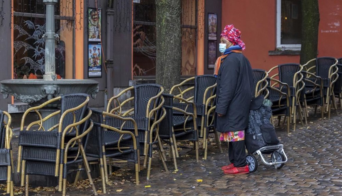 امرأة تمر قرب شرفة فارغة لمقهى في حي مارول في بروكسيل (17 ت2 2021، أ ب). 