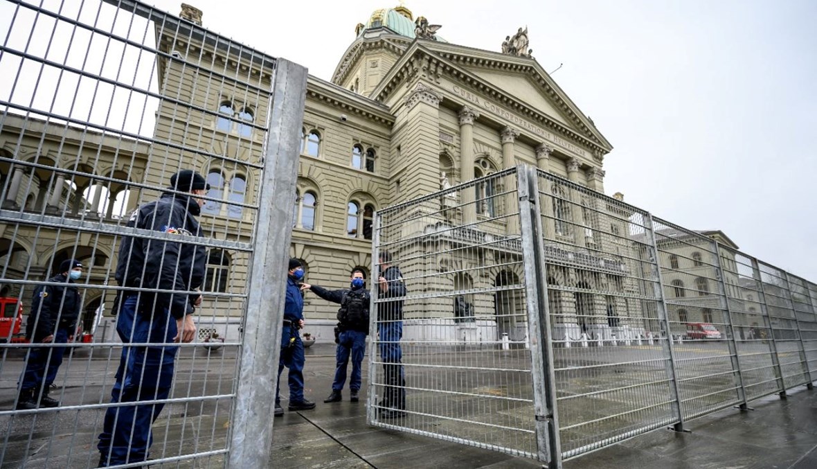 رجال الشرطة يغلقون سياجًا قرب مجلس النواب السويسري في برن قبل اعلان نتيجة التصويت على قانون كوفيد-19 (28 ت2 2021- أ ف ب). 