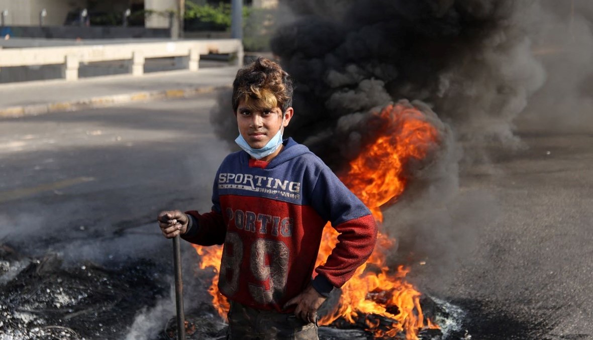 فتى لبناني يقف بجانب إطارات محترقة خلال تظاهرة في العاصمة بيروت (29 ت2 2021، أ ف ب). 