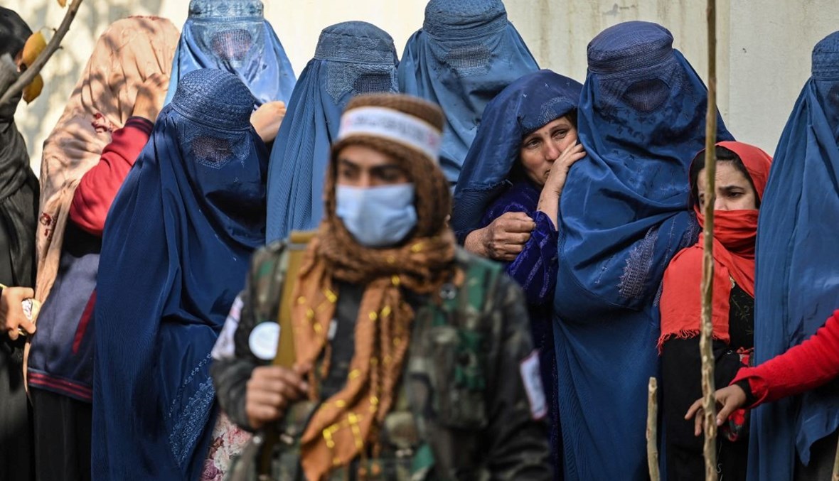 مقاتل من طالبان يقف قرب نساء انتظرن في طابور خلال توزيع مساعدات نقدية من برنامج الغذاء العالمي في كابول (29 ت2 2021، أ ف ب). 