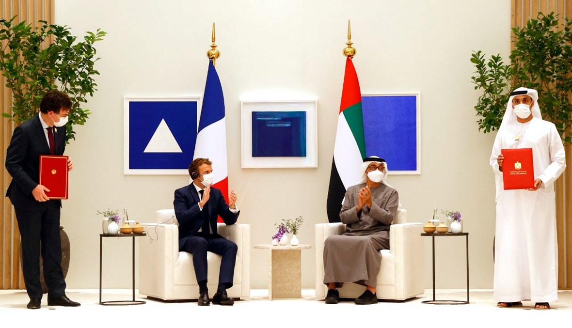 ماكرون ومحمد بن زايد مصفقين، بينما حمل شخصان اتفاقيات ثنائية وقعتها فرنسا والإمارات في دبي (3 ك1 2021، أ ف ب).