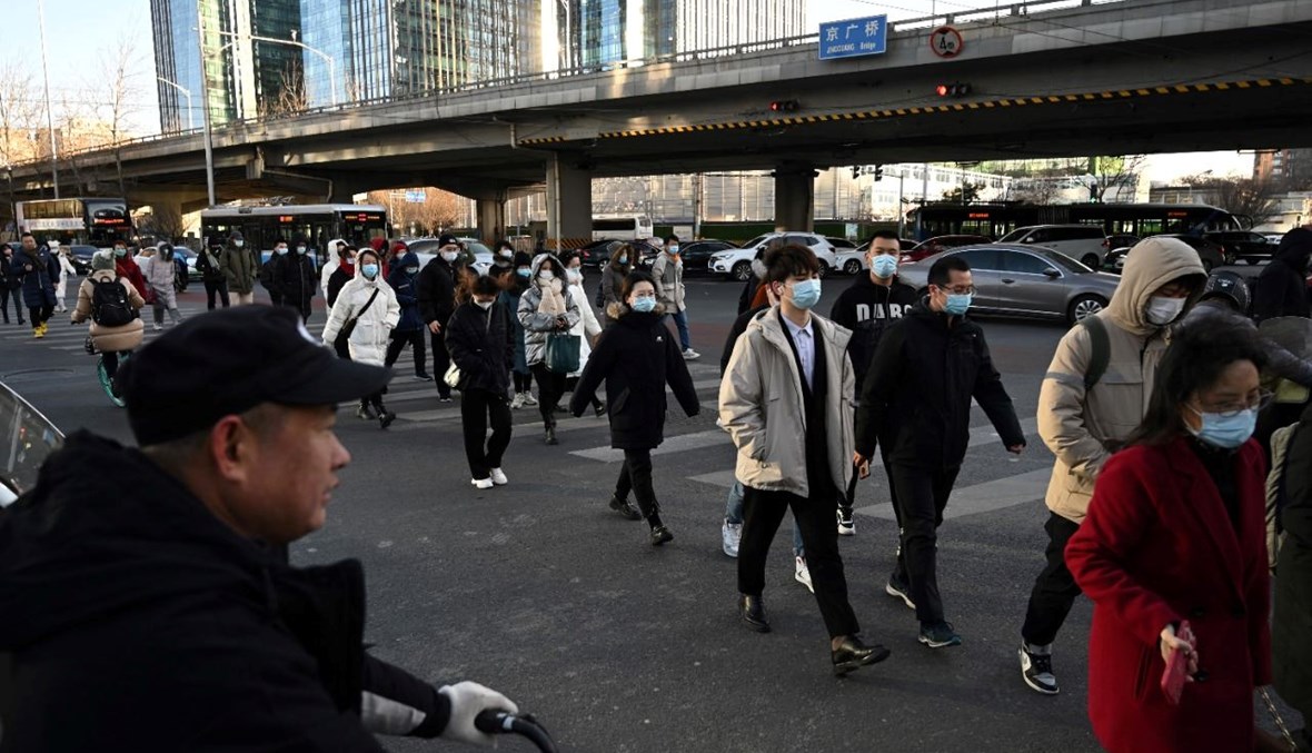 أشخاص يعبرون طريقًا في منطقة الأعمال المركزية في بيجينغ (16 ك1 2021، أ ف ب).