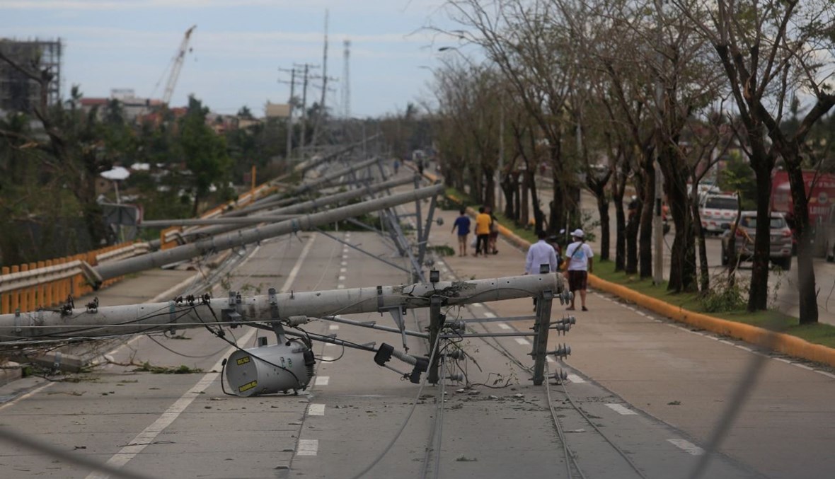 اشخاص يمرون قرب أعمدة كهربائية سقطت على الارض في بلدة تاليساي بمقاطعة سيبو من جراء الاعصار (17 ك1 2021، أ ف ب). 