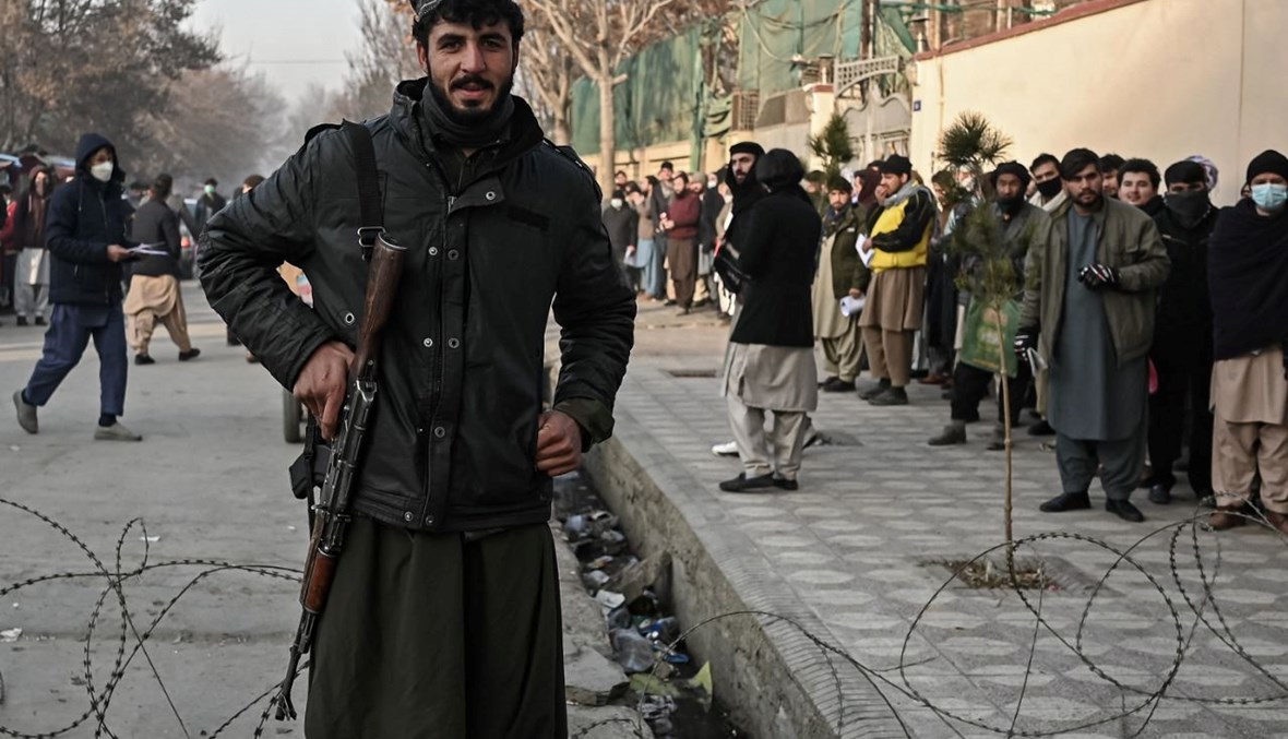 مقاتل من طالبان يقف عند نقطة تفتيش، بينما يصطف اشخاص لدخول مكتب الجوازات في كابول (19 ك1 2021، أ ف ب). 