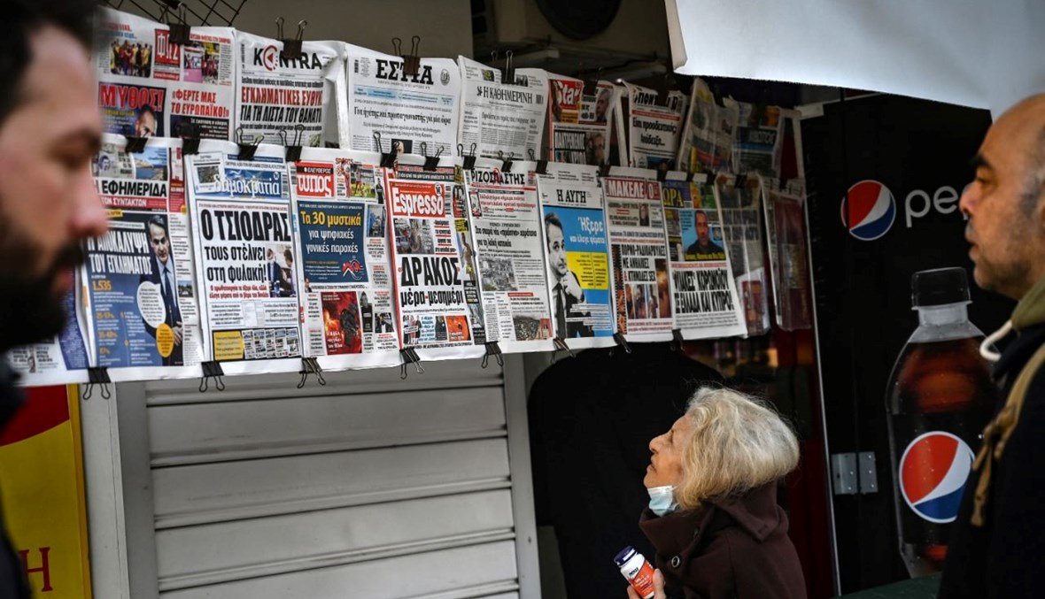 اشخاص يقرأون عناوين الصحف في كشك في أثينا (16 ك1 2021، ا ف ب). 