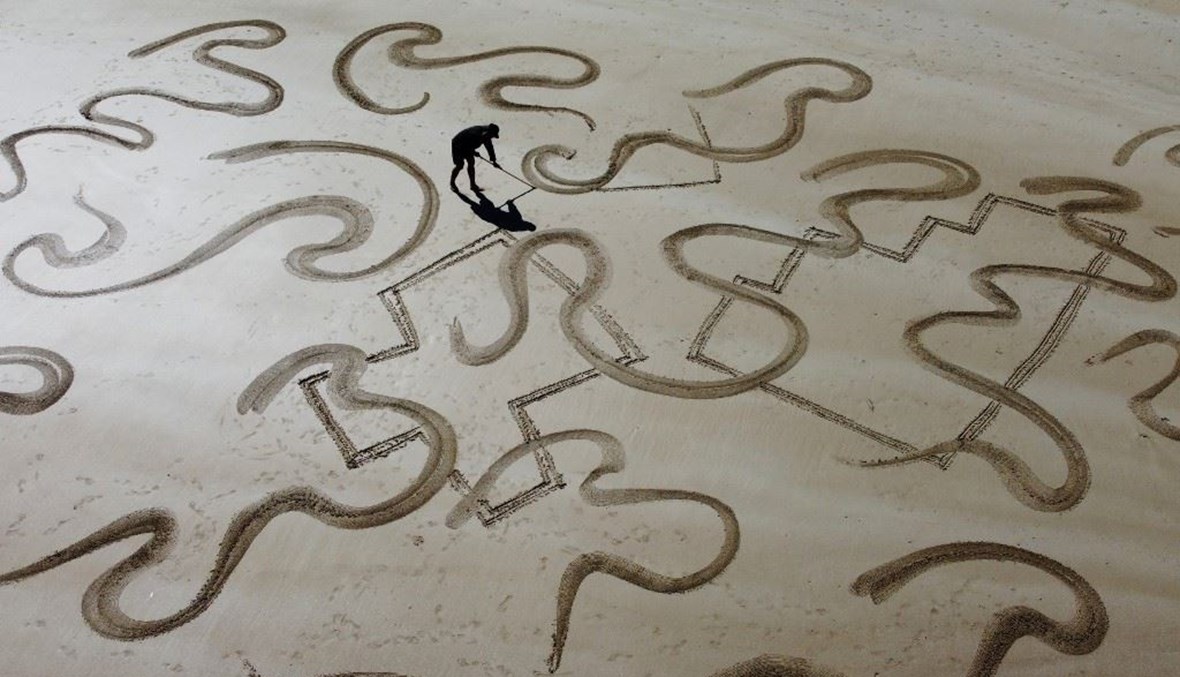  الفنان ديريك يونغ وهو يصنع رسمًا رمليًا واسع النطاق على شاطئ ساي وان في منطقة ساي كونغ في هونغ كونغ (أ ف ب). 