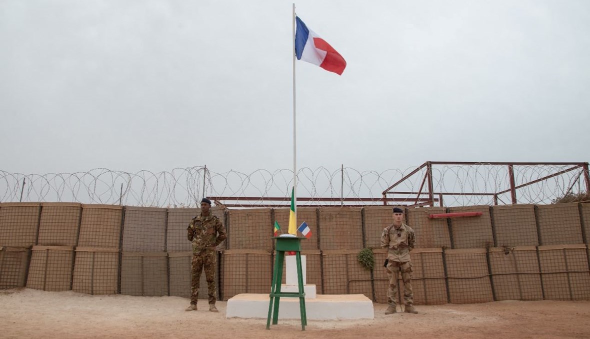 جنديان مالي وفرنسي يقفان قرب سارية العلم في معسكر برخان قبل مراسم تسليم قاعدة برخان العسكرية الى الجيش المالي في تمبكتو (14 ك1 2021، أ ف ب). 